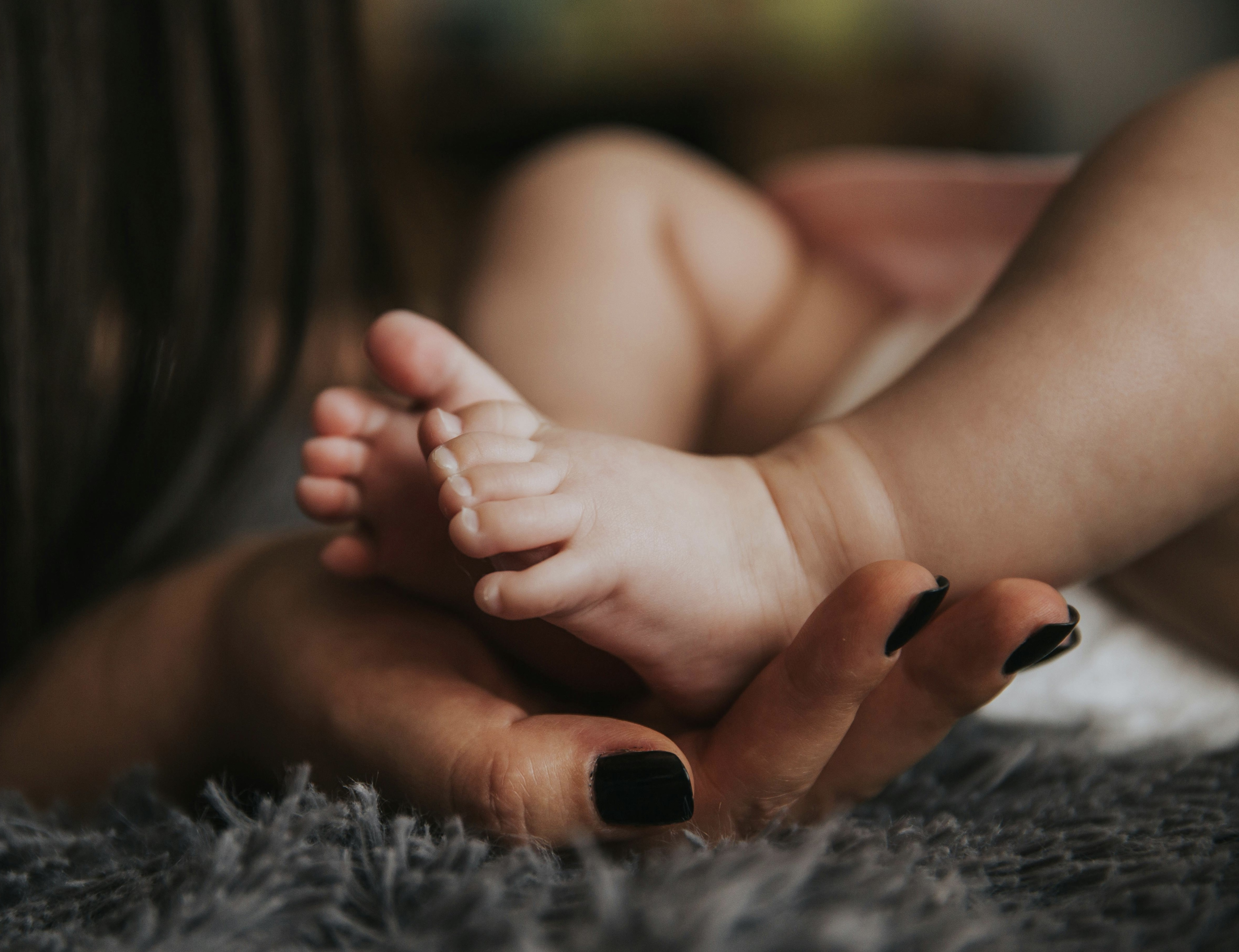 A doula's hand holding an infant's feet in their palm. Doulas provide comfort, education, and care to newborns. 